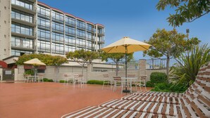 Une cour d’hôtel avec des espaces de détente en plein air, comprenant des chaises longues et des tables, et un bâtiment avec de nombreux balcons en arrière-plan.
