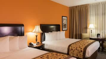 A hotel room with two beds, a nightstand with a lamp, a chair, and a table with a lamp.