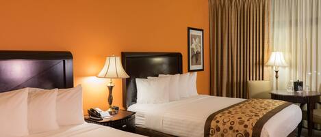 A hotel room with two beds, a nightstand with a lamp, a chair, and a table with a lamp.