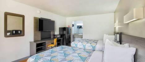 Habitación de hotel con dos camas, un televisor, un escritorio y un espejo.