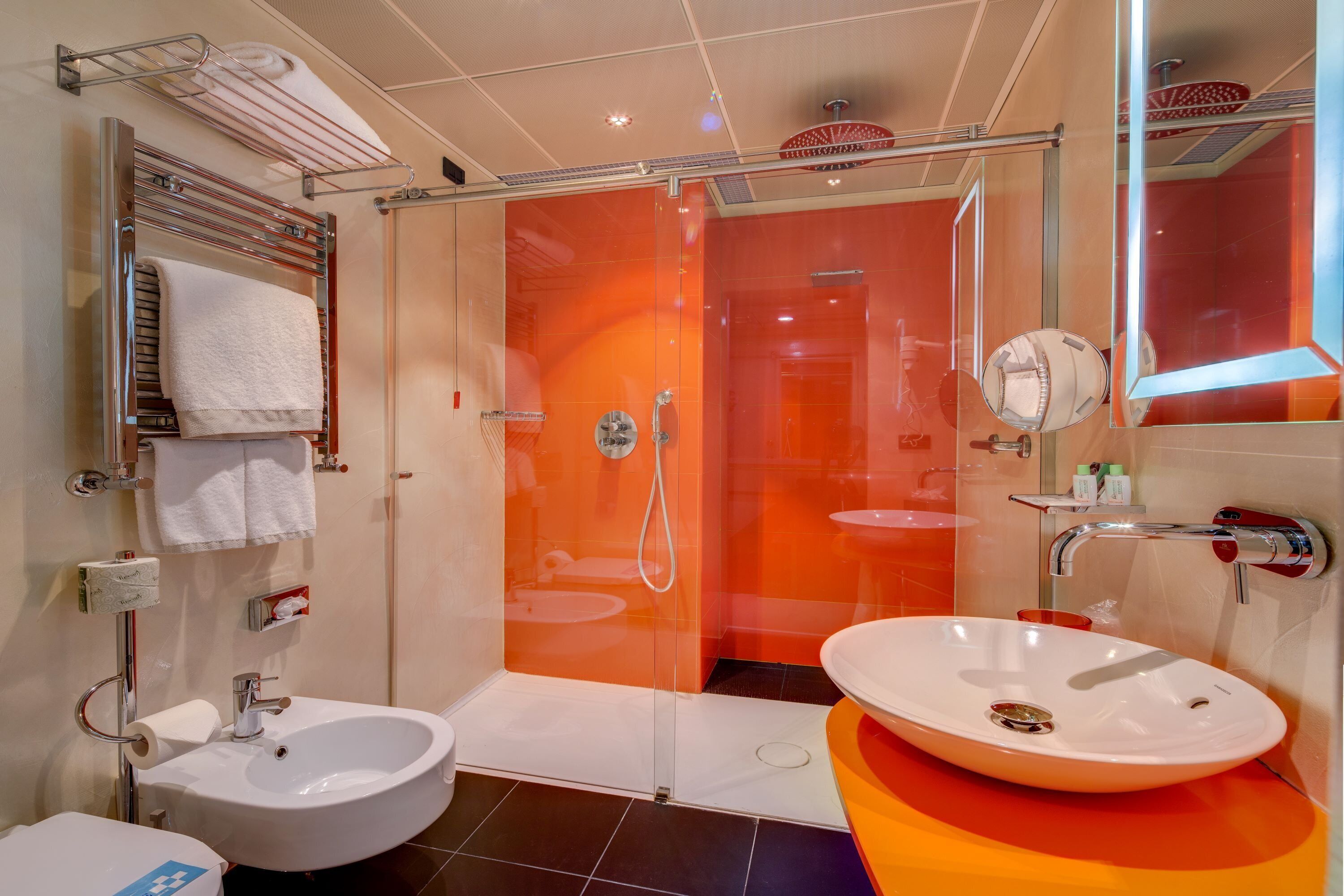Un baño moderno con ducha envuelta en vidrio, dos lavamanos y un espejo grande.