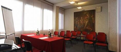Un salón de conferencias con una mesa roja, sillas, un proyector y un cuadro en la pared.