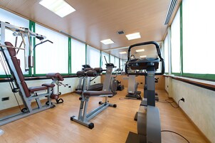 A gym with various exercise equipment, large windows, and wooden floors.