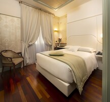 A neatly arranged bedroom with a large bed, a chair, a bedside table with a lamp, and a vase with flowers.