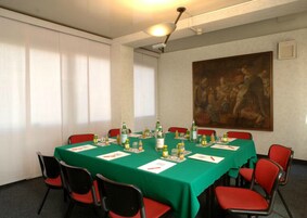 Una sala conferenze con un tavolo verde, sedie rosse e un quadro appeso al muro.