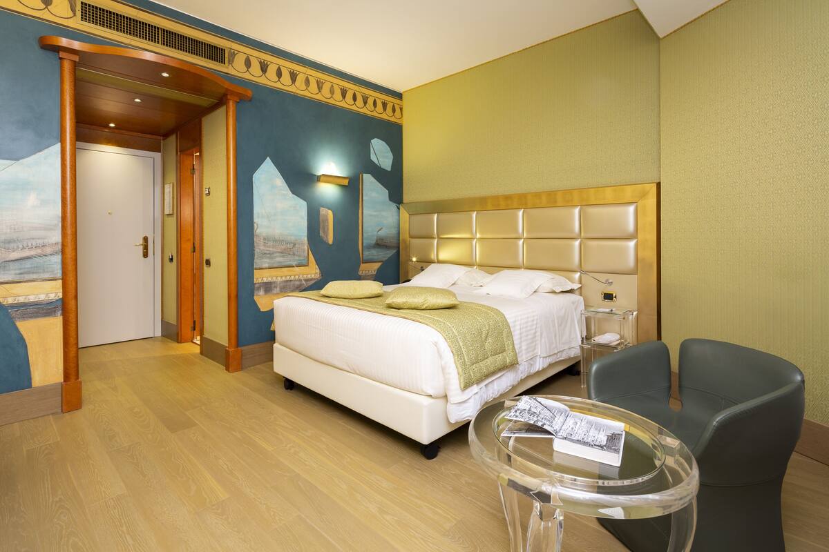 A hotel room with a large bed, a small table, a chair, and a door leading to another room.