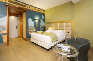 Una habitación de hotel con una cama grande, una mesita pequeña, una silla y una puerta que da a otra habitación.