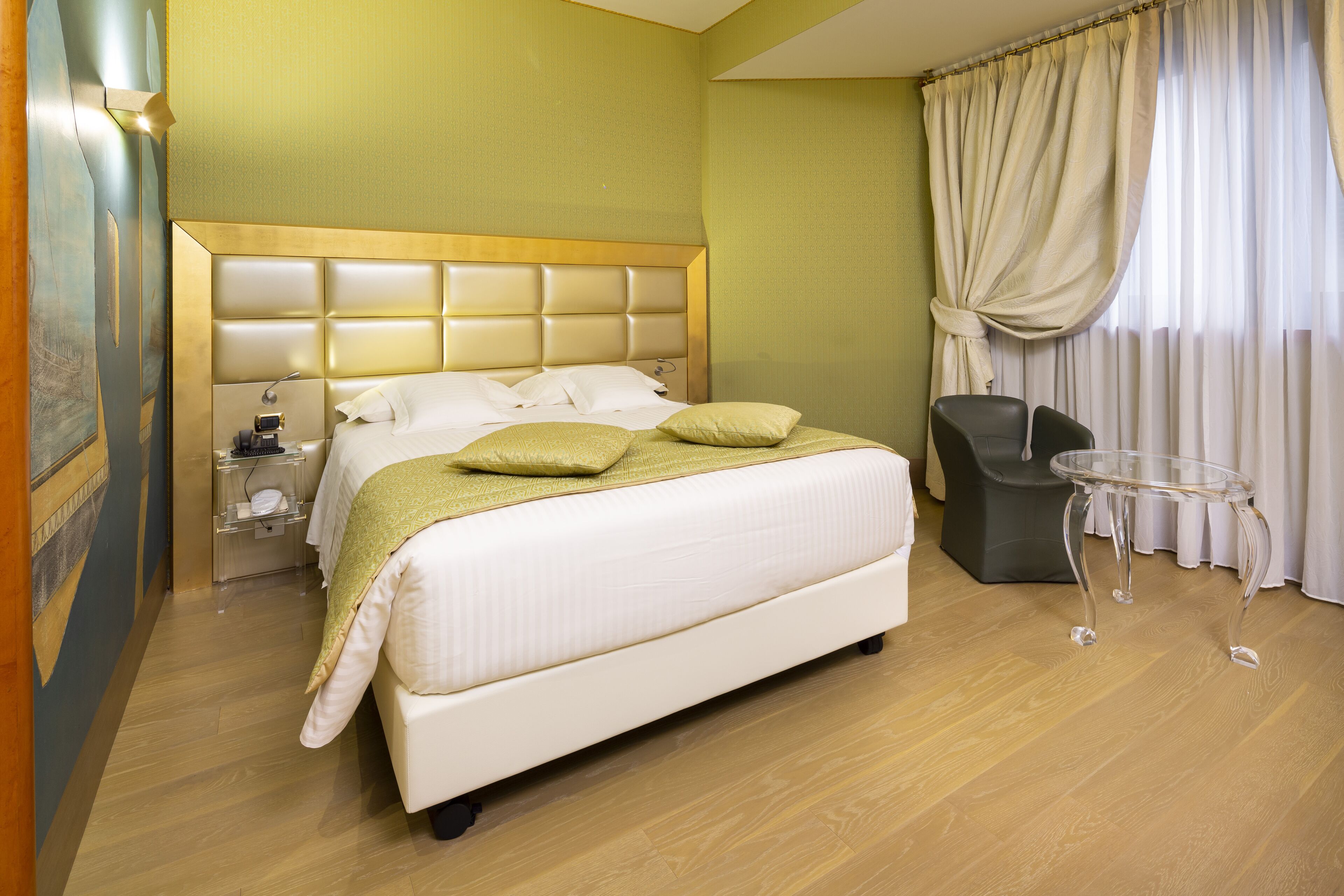 A hotel room with a large bed, a bedside table, a chair, and a glass table.