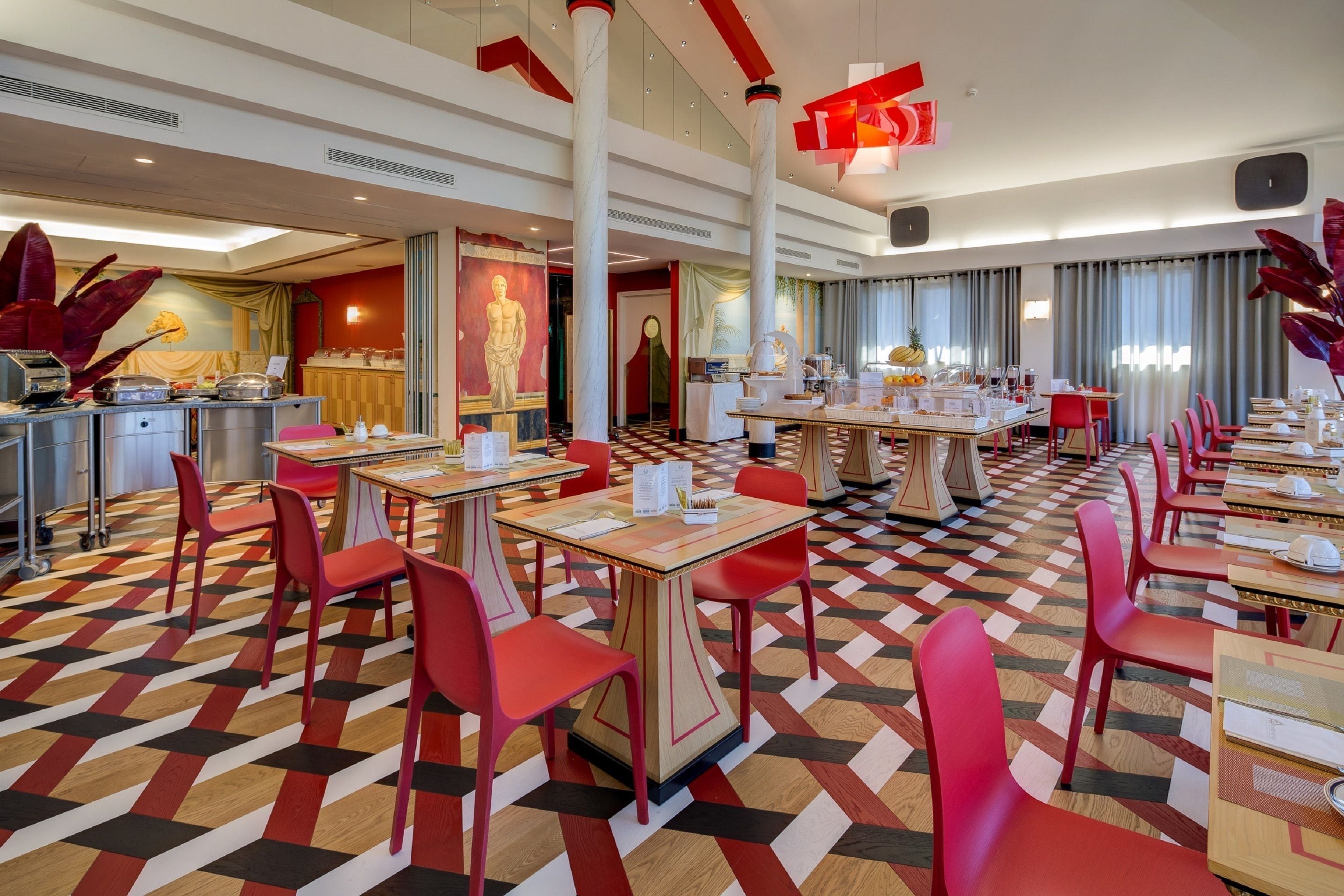 A hotel dining area with multiple tables and chairs, a check-in counter, and a large mural on the wall.