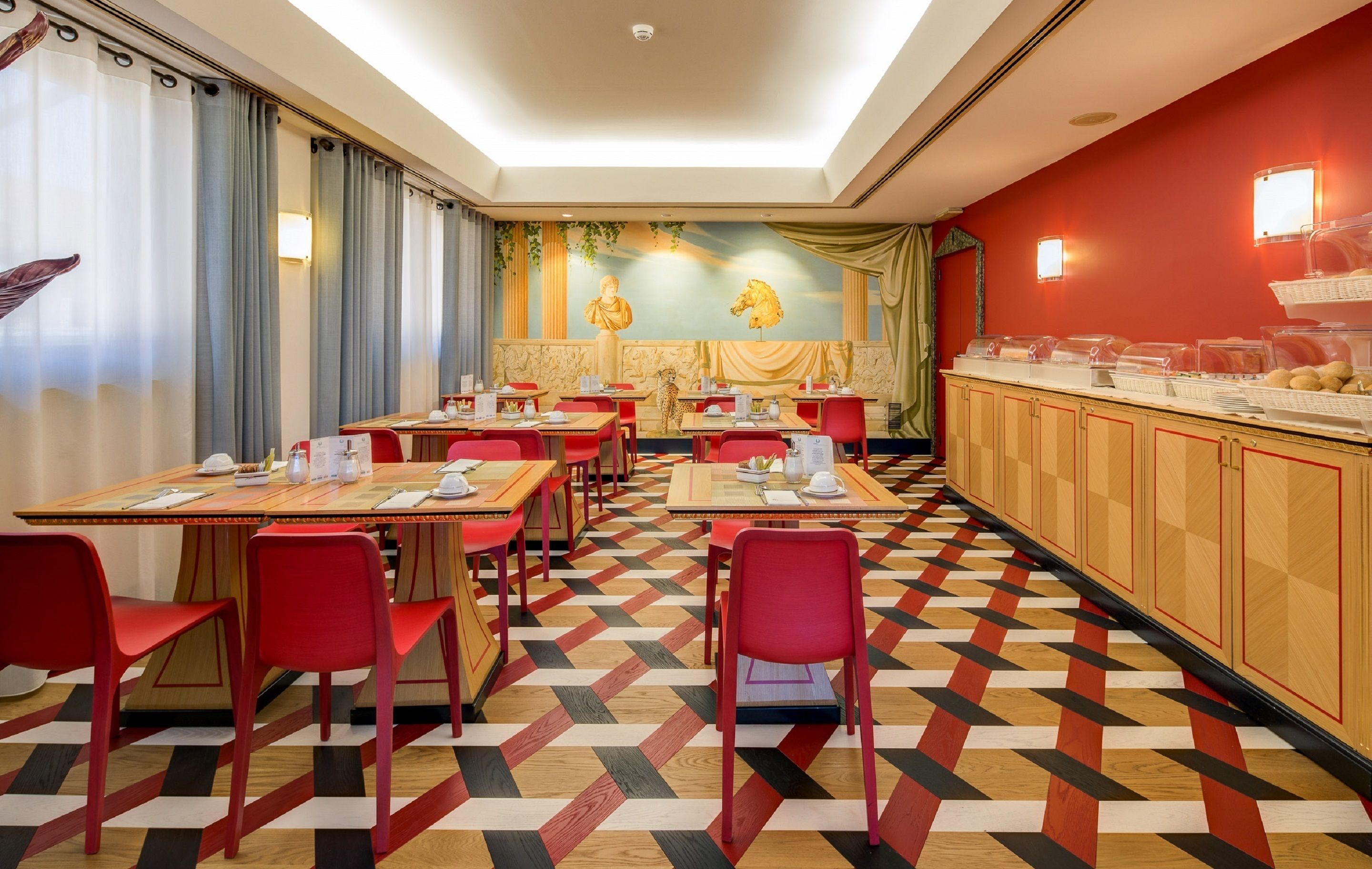 A restaurant with red chairs and tables, a patterned floor, and a buffet area with food containers.