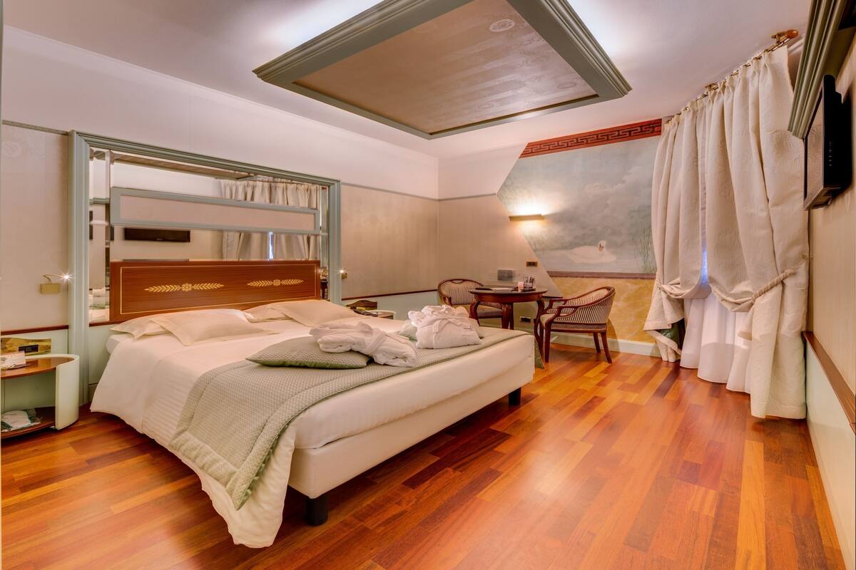 A hotel room with a large bed, a desk, a chair, and a view of the outdoors.