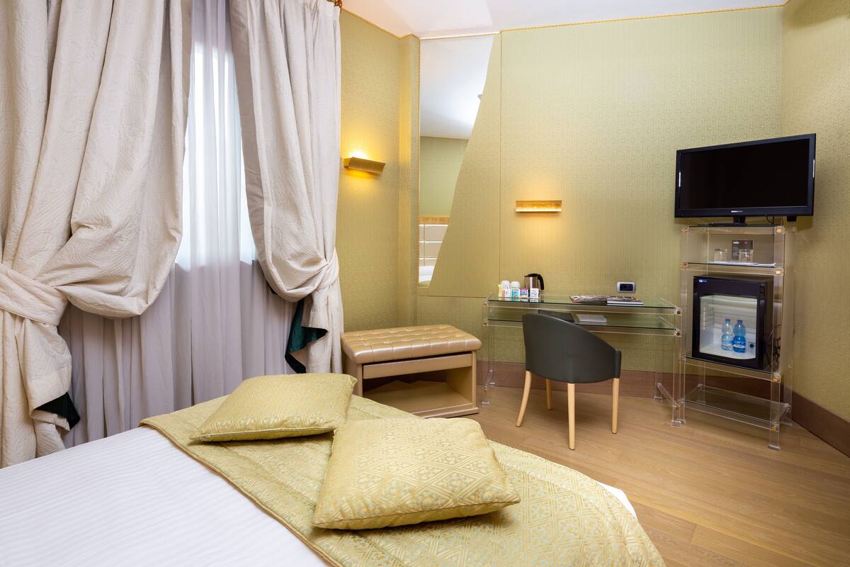 A hotel room with a bed, a desk, a chair, a television, and a minibar.
