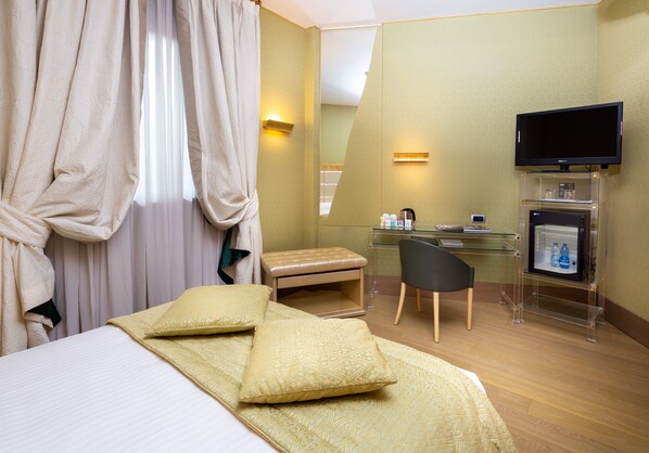 Una habitación de hotel con cama, escritorio, silla, televisor y minibar.