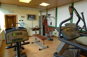 Een sportschool met cardioapparatuur, gewichten en een bank.