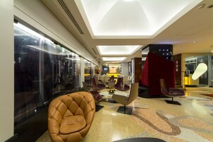 Een moderne hotelentree met een centrale zithoek, een groot raam en een rode scheiding.'