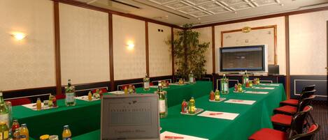 Un salón de conferencias con una mesa verde, computadoras portátiles y diversas bebidas.