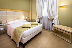 Een keurig ingerichte hotelkamer met een groot bed, nachtkastjes, een bankje en een wandlamp.
