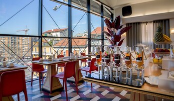 Un ristorante moderno con terrazza panoramica, sedie rosse e un buffet con frutta e bevande.