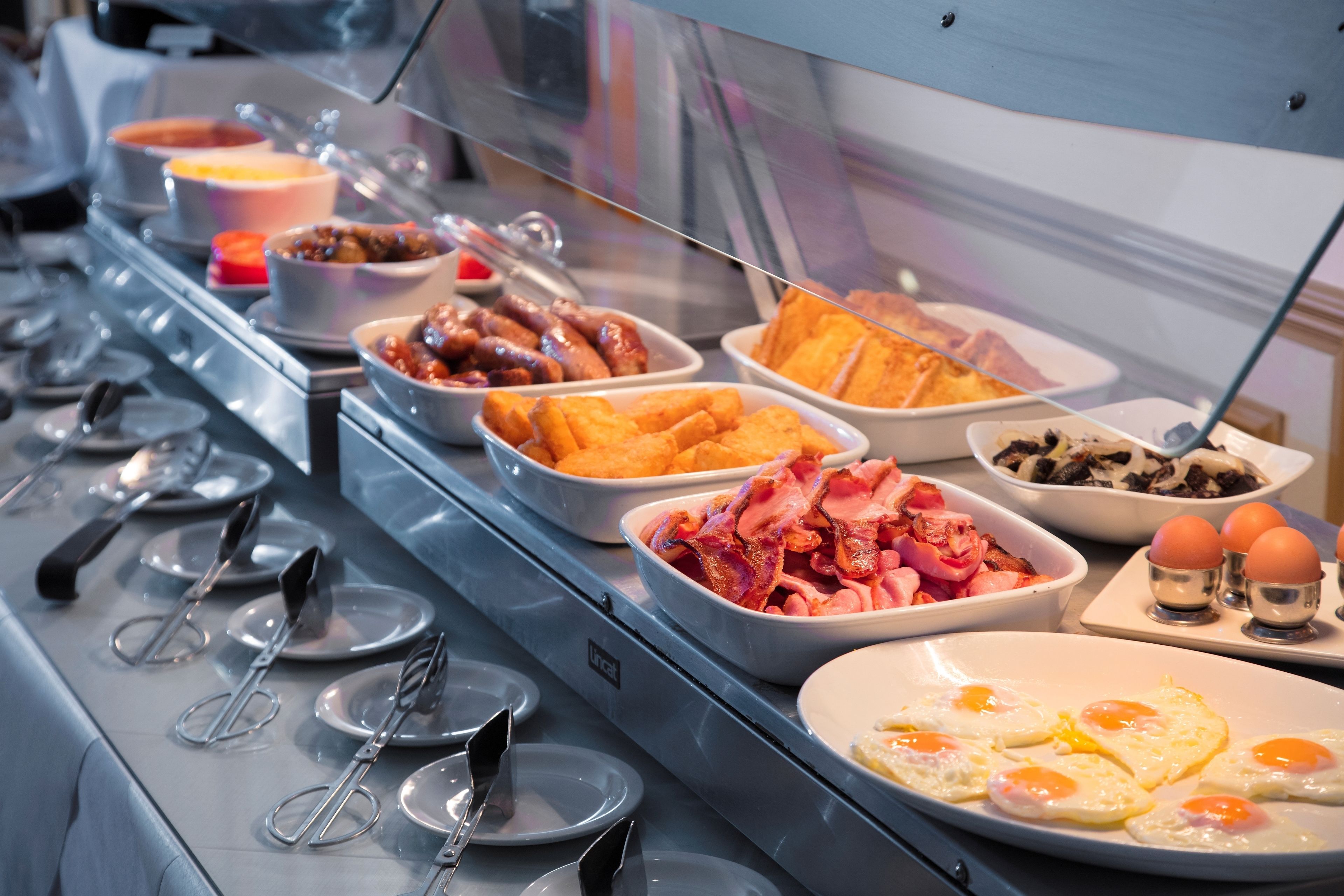 A buffet with various breakfast items including eggs, bacon, and pastries.