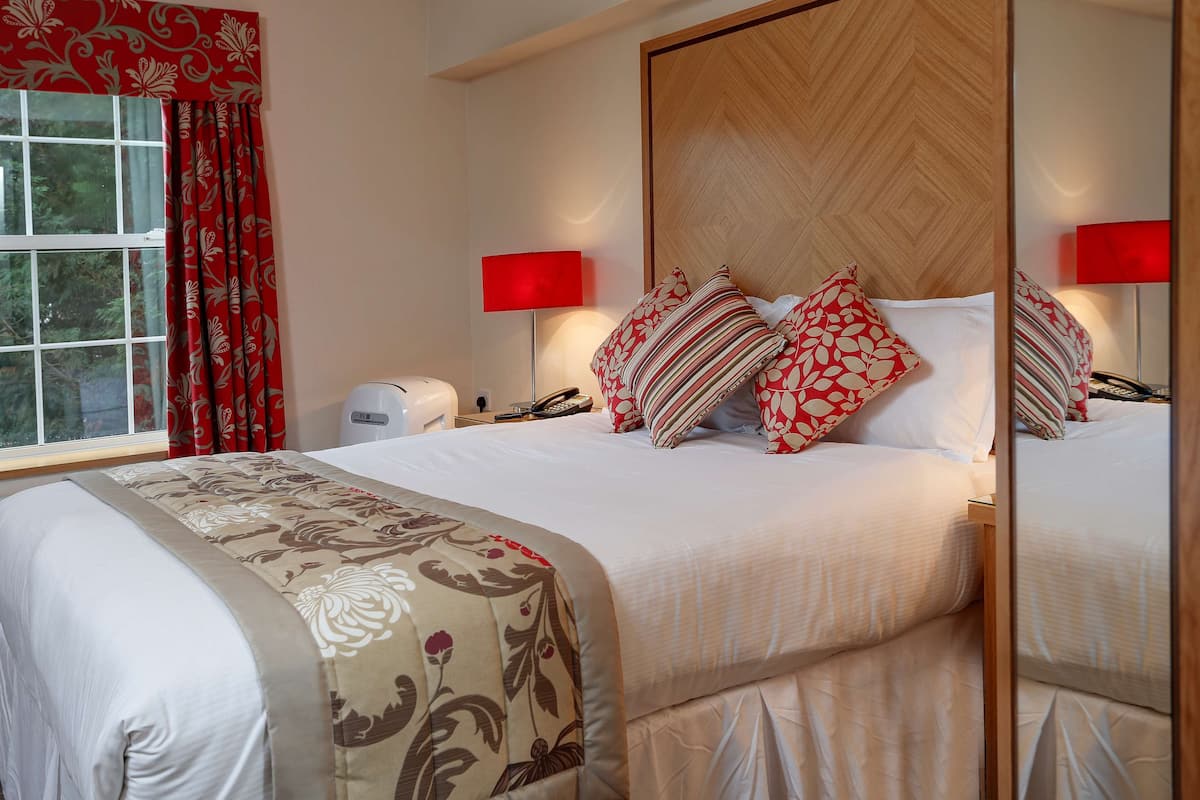 Une chambre d’hôtel avec un grand lit, deux tables de chevet, une commode, un miroir et une fenêtre avec des rideaux rouges.