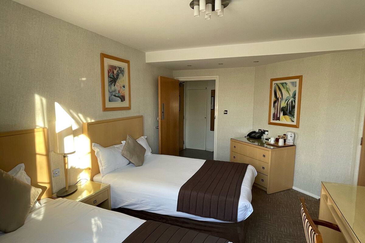 Une chambre d’hôtel avec deux lits, un bureau, une commode et une porte donnant sur une autre pièce.