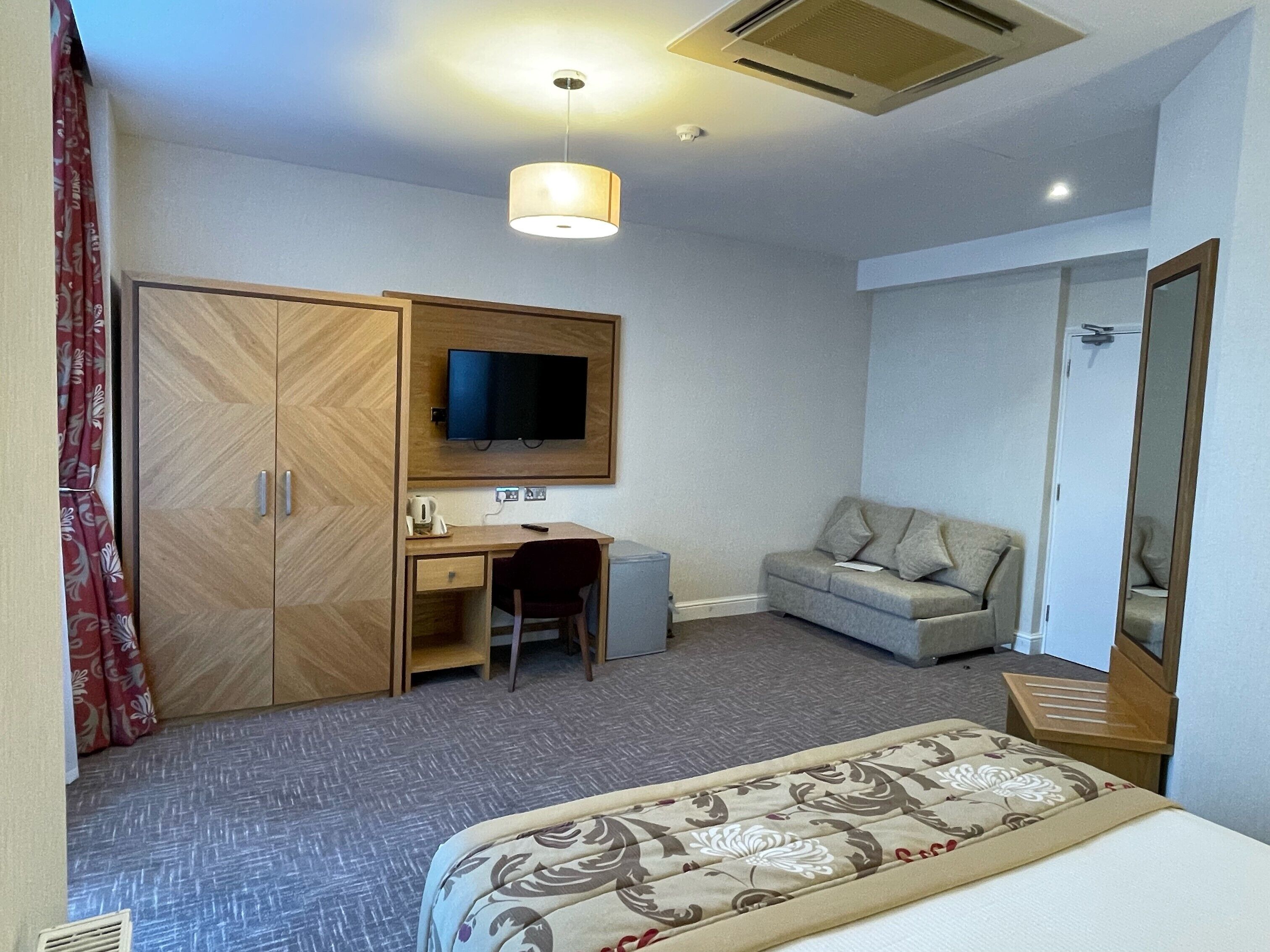 A hotel room with a bed, a desk, a television, a wardrobe, and a sofa.