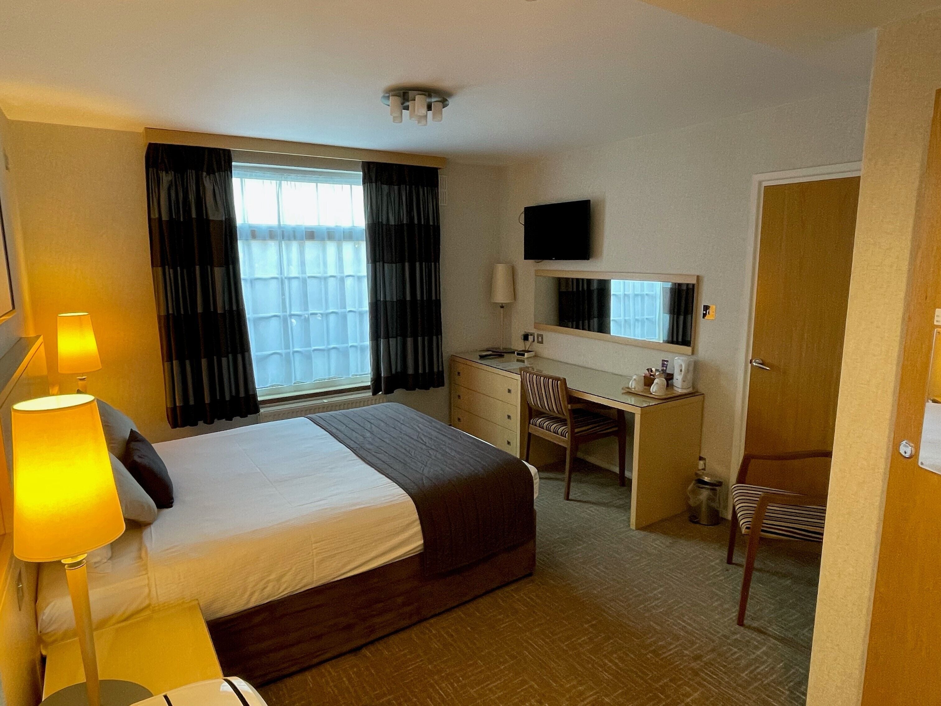 A hotel room with a bed, desk, chair, and a television.