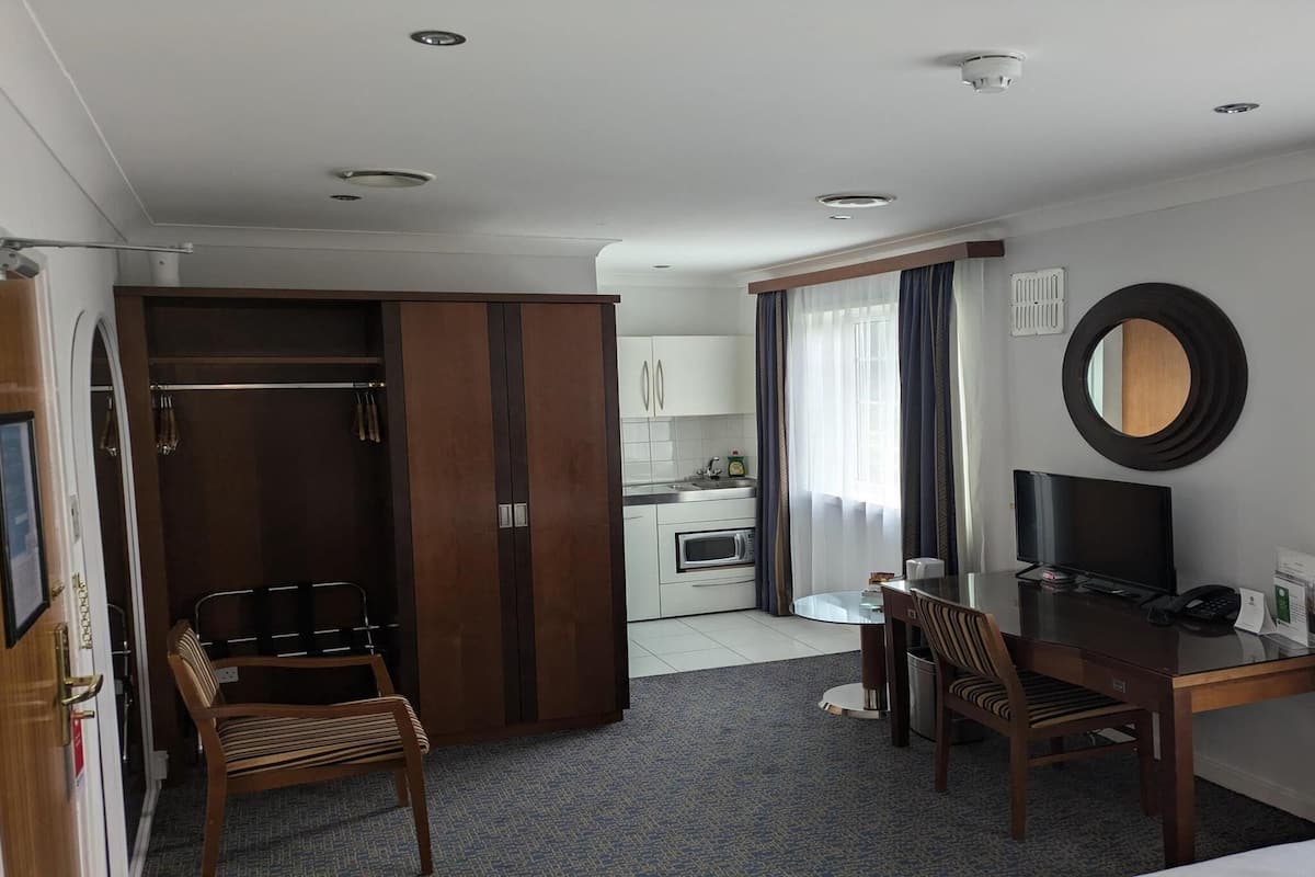 Une chambre d’hôtel comprenant un lit, un bureau avec une chaise, une télévision, une petite kitchenette et une armoire.