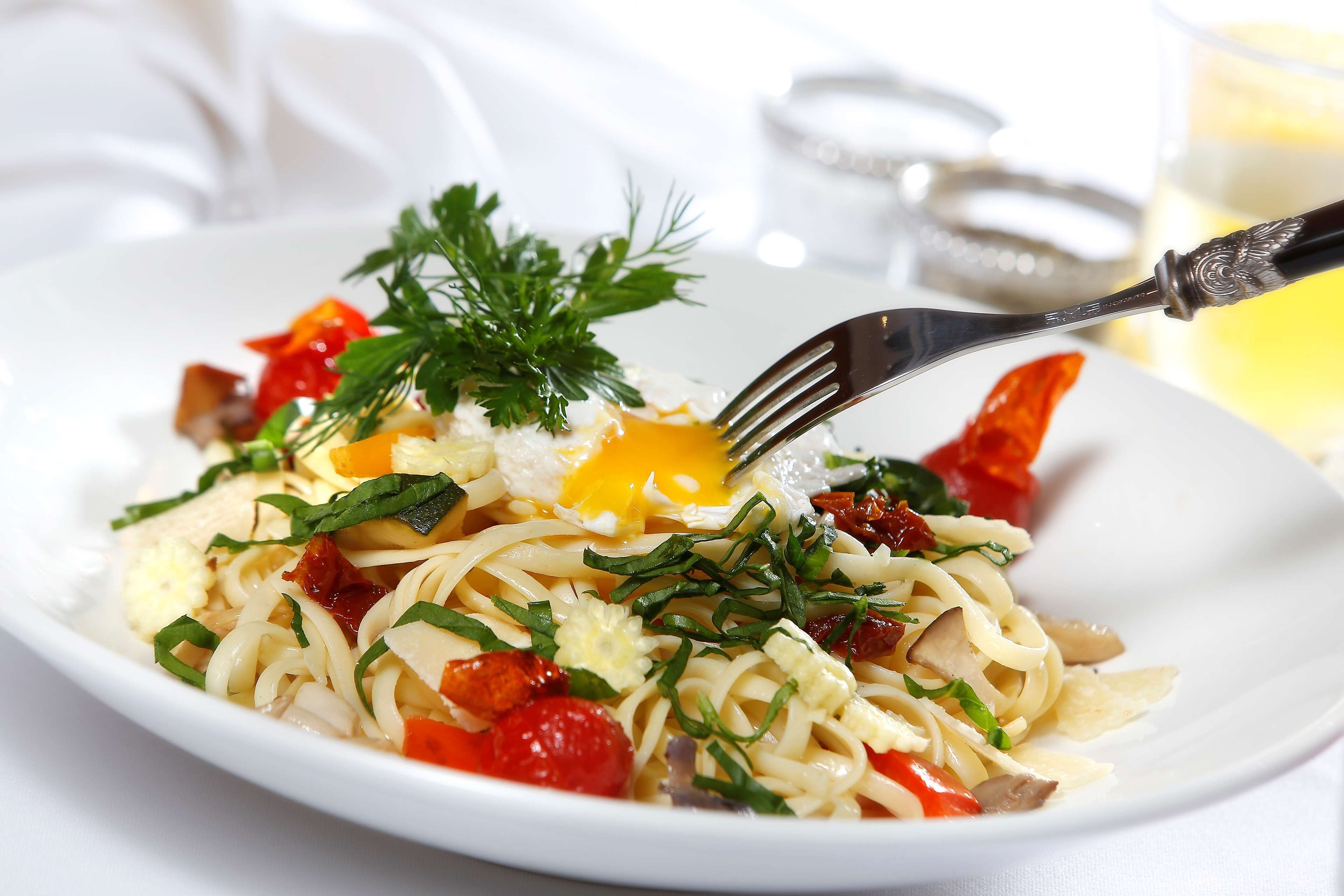 A plate of pasta with various toppings including a poached egg, tomatoes, and herbs.