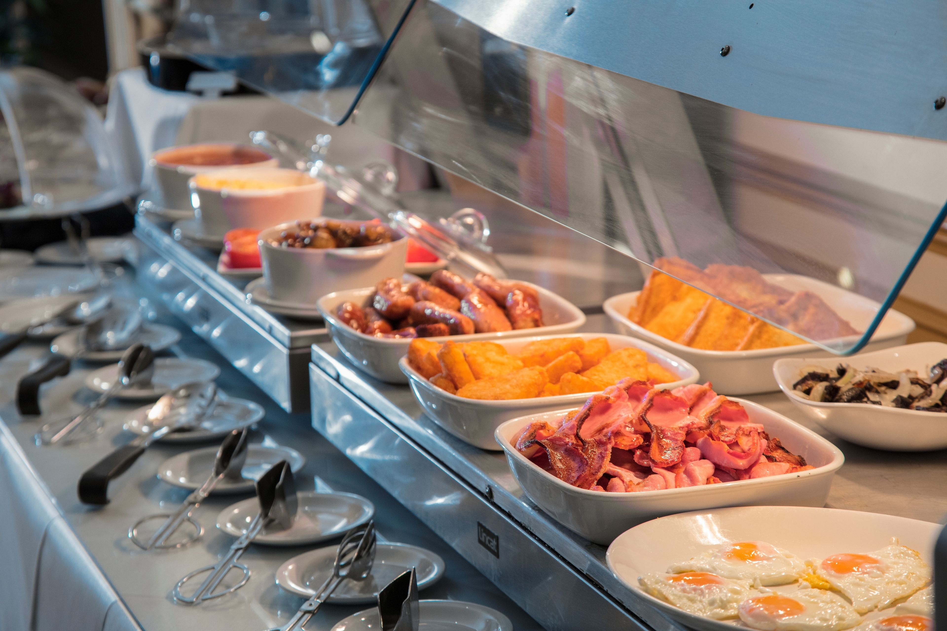 A buffet with various breakfast items including eggs, bacon, and pastries.