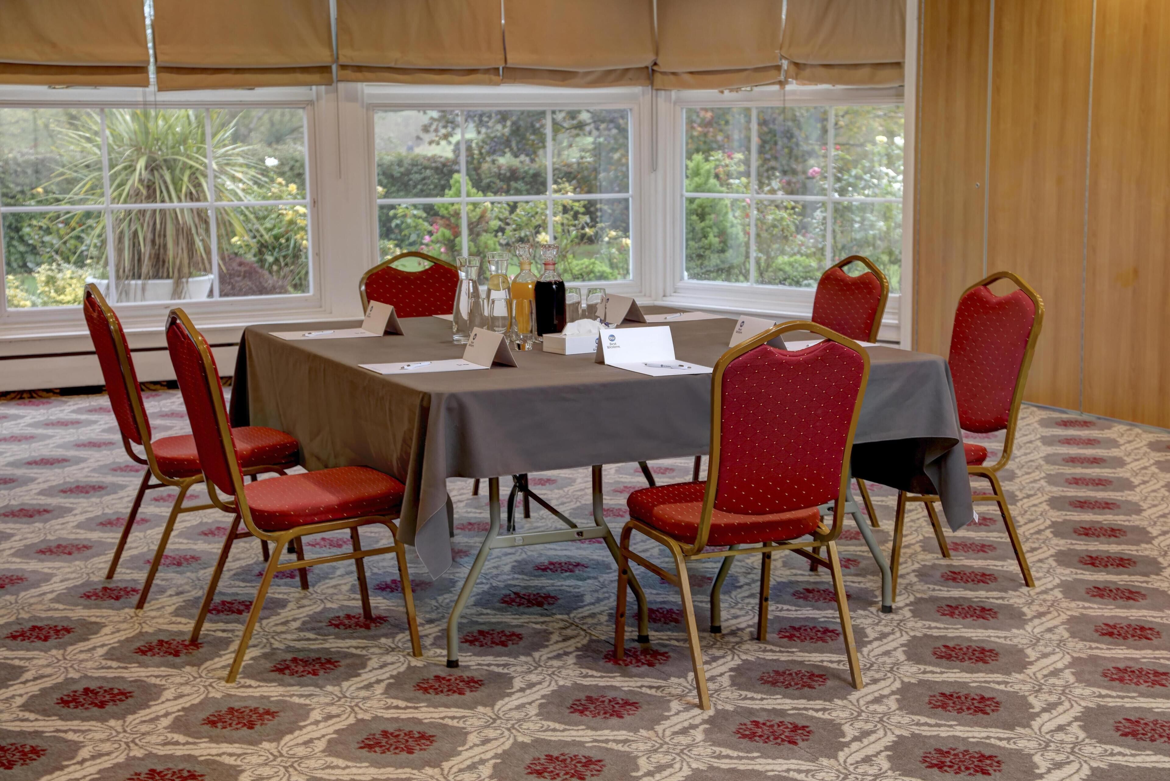 A conference room with a table, chairs, and a view of greenery through large windows.
