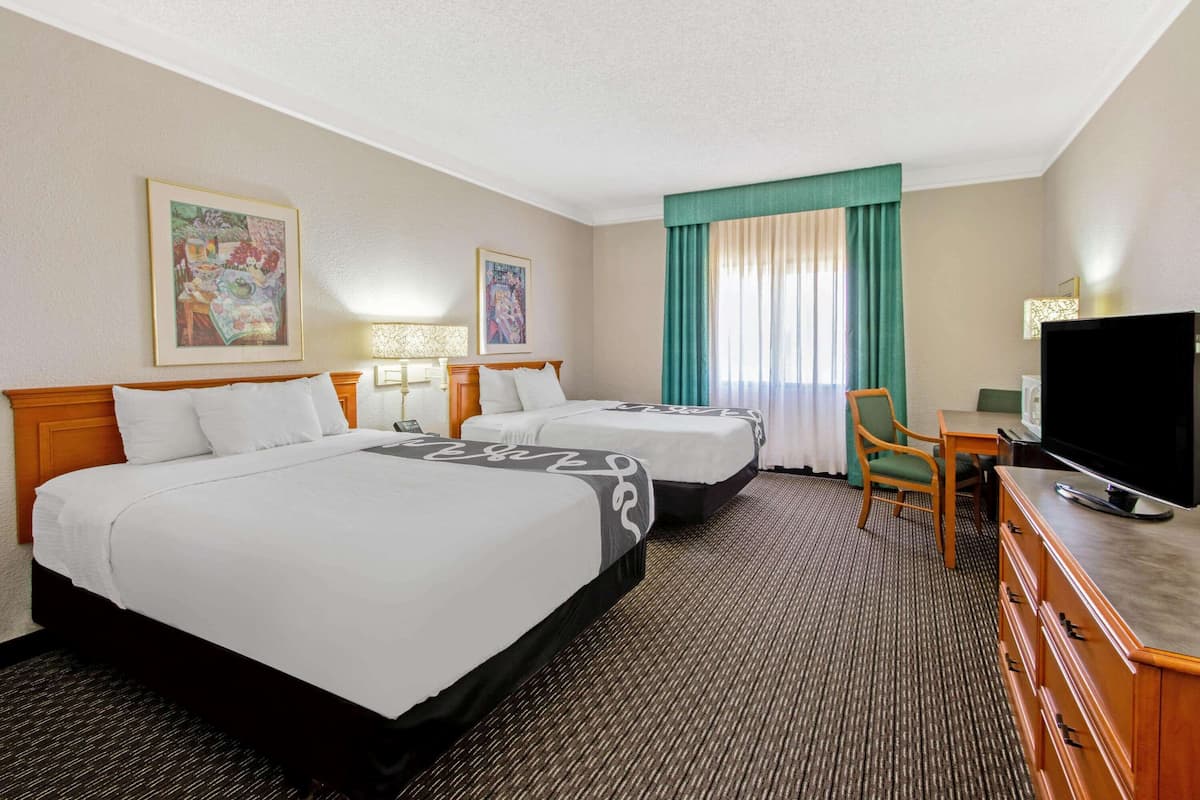 Ein Hotelzimmer mit zwei Betten, einem Schreibtisch mit Fernseher und einem Sessel.