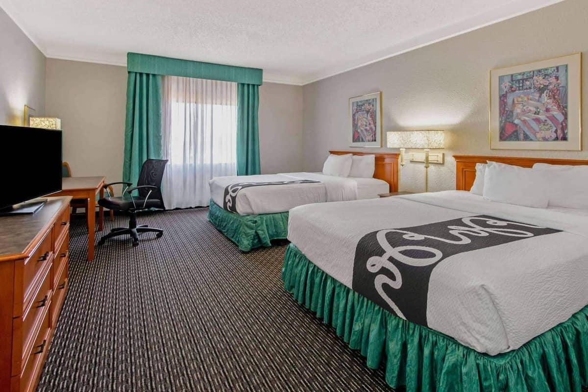 Ein Hotelzimmer mit zwei Betten, einem Schreibtisch mit Fernseher, einem Sessel, einer Lampe und Bildern an den Wänden.