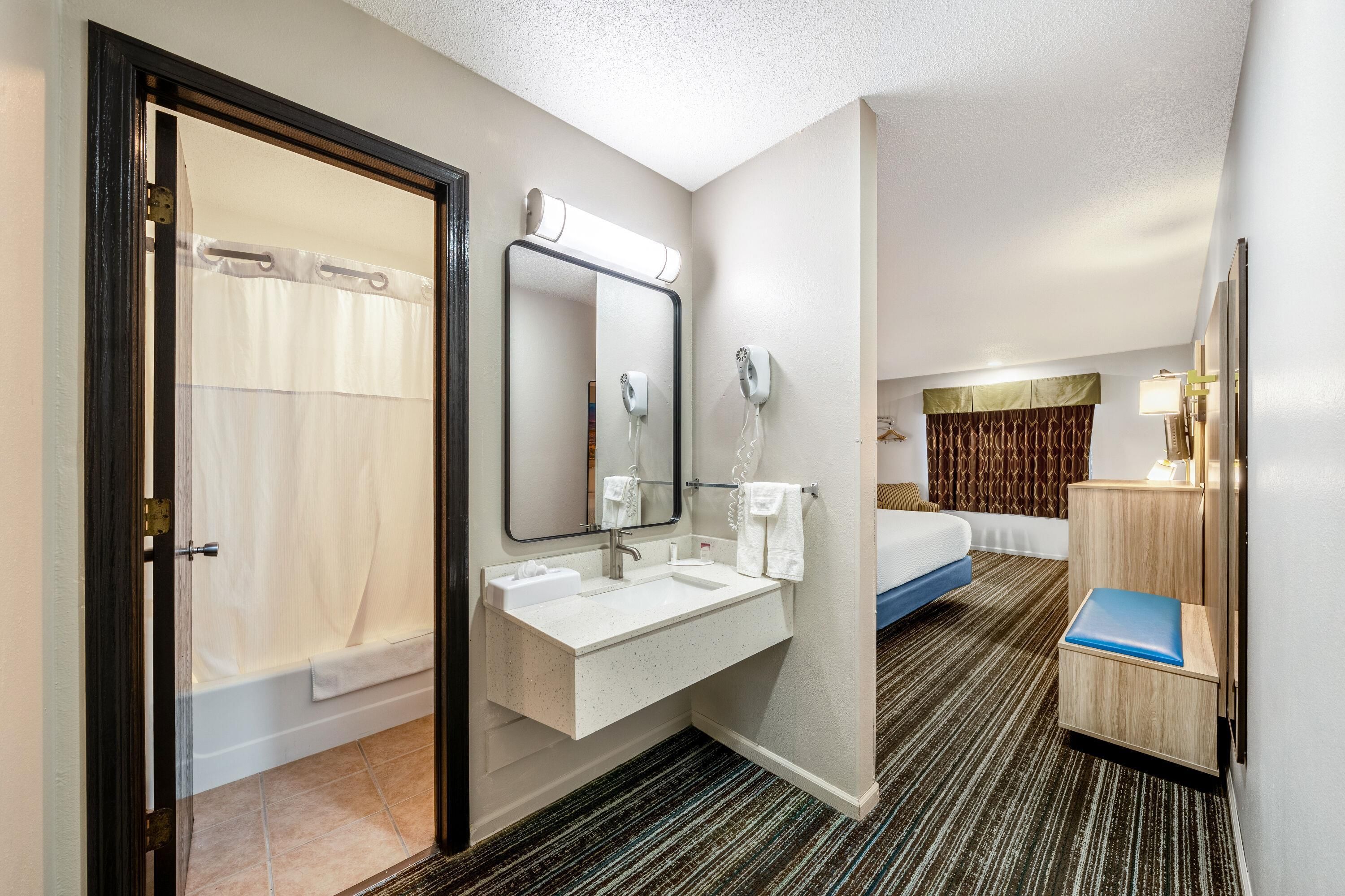 A hotel room with a bathroom, a bed, a bedside table, and a mirror.