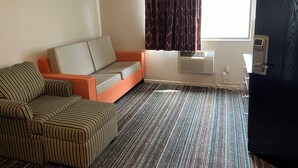Een hotelkamer met een gestreepte bank, een kleine tafel, een raam met gordijnen, een airconditioning en een deur.