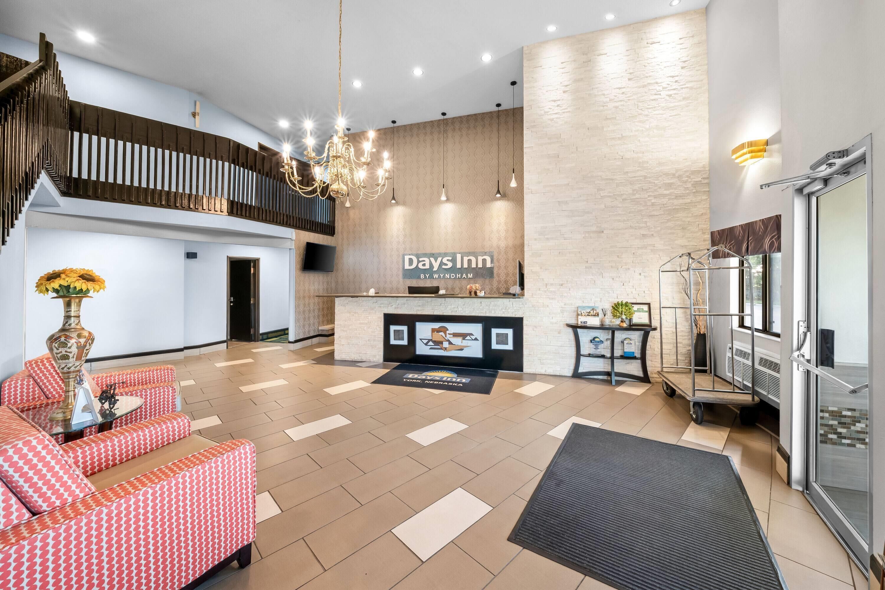 Een hotel lobby met een receptiebalie, een kroonluchter, gestreepte banken en een trap.