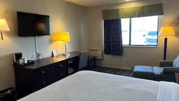 A hotel room with a bed, desk, chair, lamps, TV, and a window with curtains.