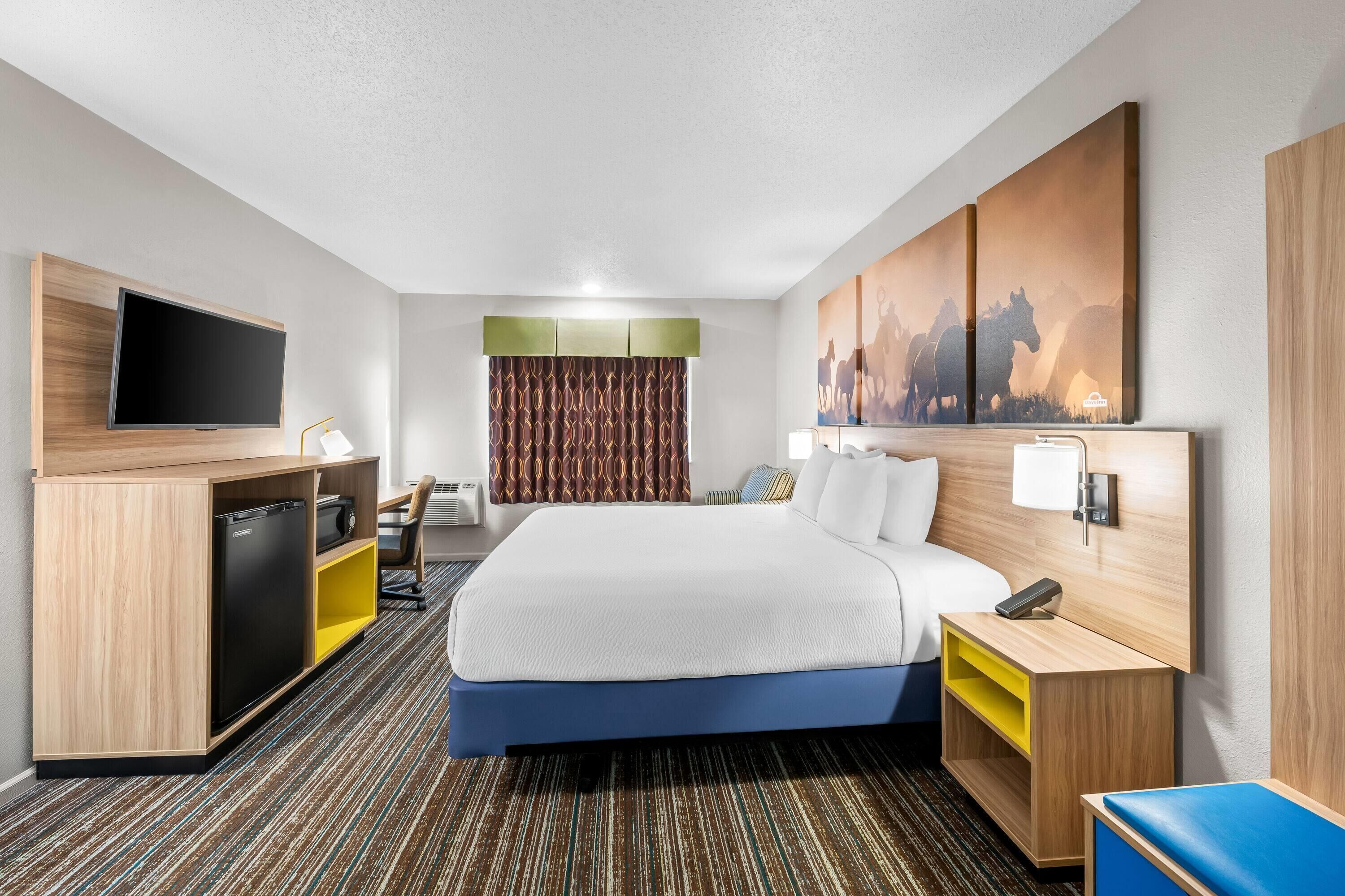 A hotel room with a bed, a desk, a television, a wardrobe, and a painting on the wall.