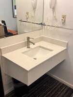 A bathroom with a rectangular sink, a mirror, and a hairdryer mounted on the wall.