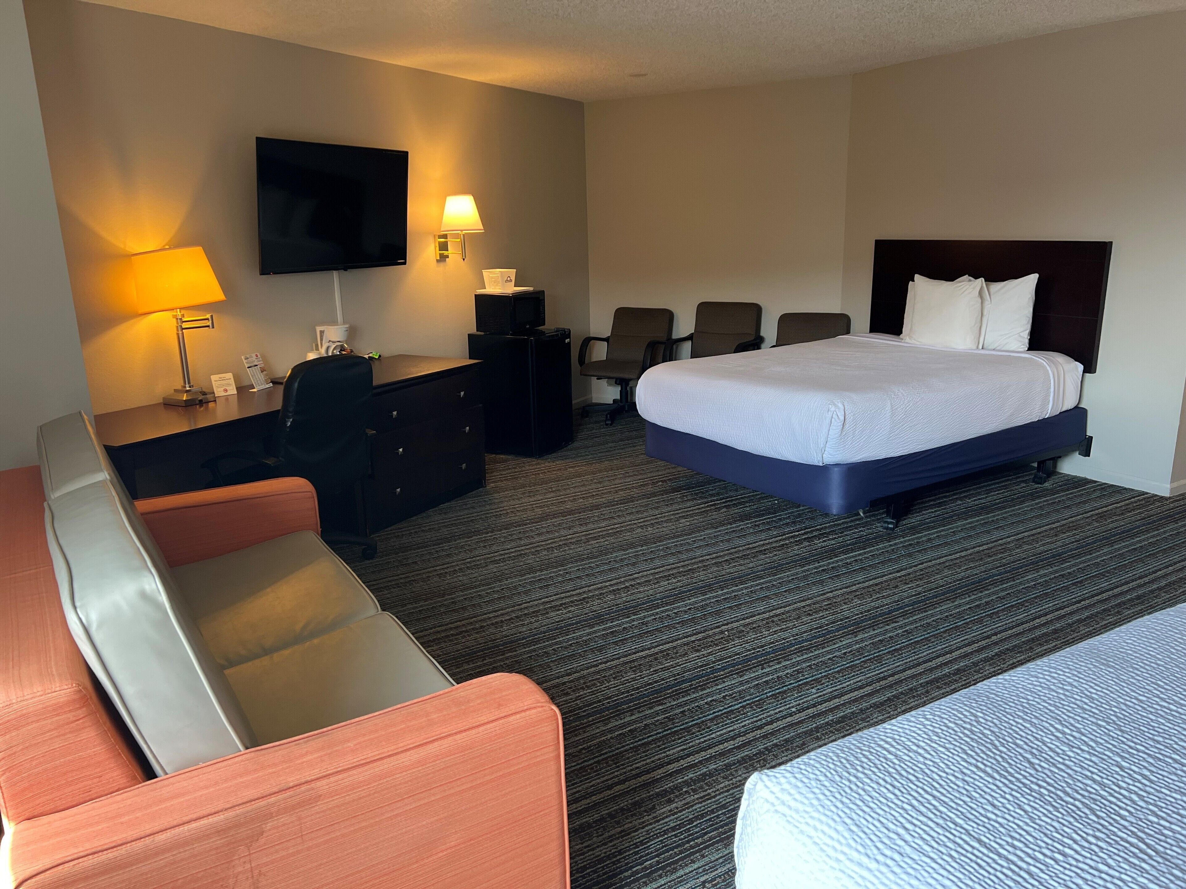A hotel room with a bed, a desk, a television, and a seating area.
