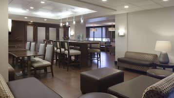 Un vestíbulo de hotel con zona de comedor, arreglos de asientos y un bar.