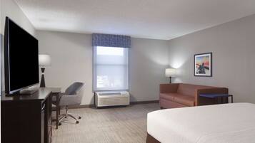 A hotel room with a bed, a desk with a TV, a chair, a window with blinds, and a painting on the wall.