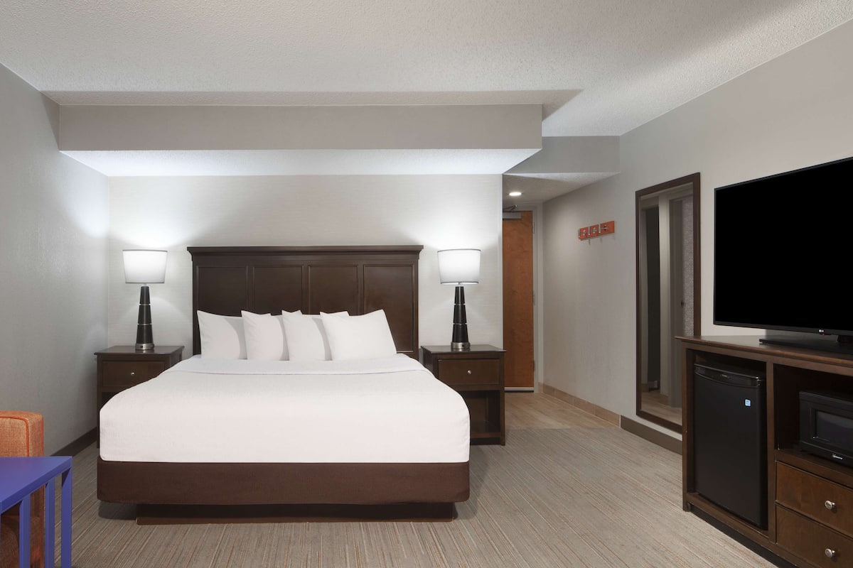 A hotel room with a large bed, two bedside tables with lamps, a television, and a small refrigerator.