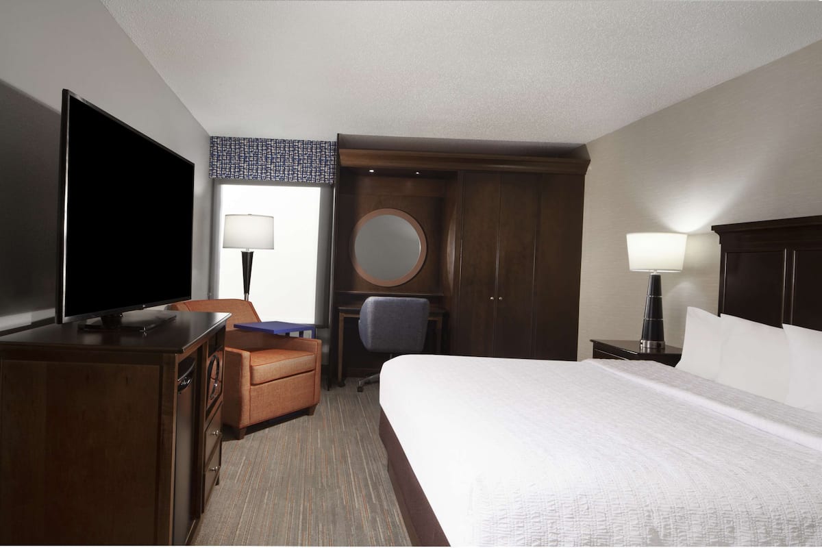 A hotel room with a bed, a TV, a desk, a chair, a wardrobe, and two lamps.