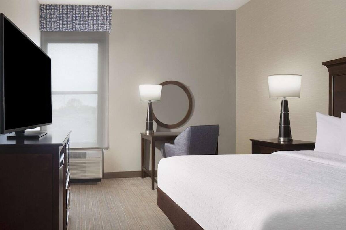 A hotel room with a bed, a TV, a desk, and two bedside lamps.