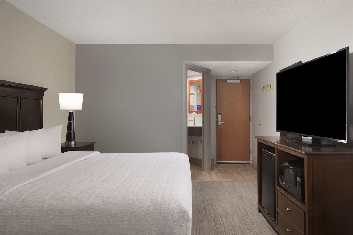 A hotel room with a bed, a TV, a lamp, and a microwave.