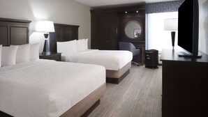 Habitación de hotel con dos camas, un escritorio, una silla, un televisor y un ventanal grande.