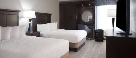 A hotel room with two beds, a desk, a chair, a television, and a large window.