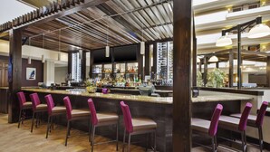 A bar area with multiple bar stools, a counter with bottles, and a wooden ceiling structure.