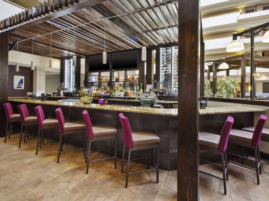 Zona bar con diversi sgabelli, un bancone pieno di bottiglie e una struttura di soffitto in legno.